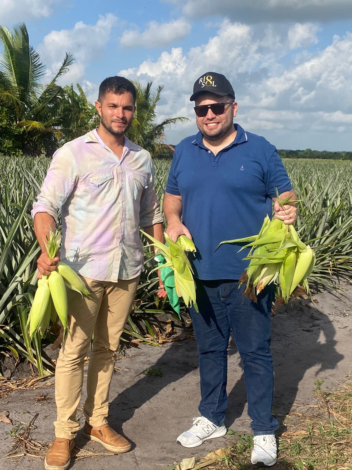 Dois produtores em área agrícola segurando espigas de milho